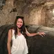 Brittany Shelley in a wine cellar wearing a white tank top, with dark hair, and sunglasses smiling