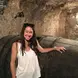 Brittany Shelley in a wine cellar wearing a white tank top, with dark hair, and sunglasses smiling
