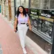 Kirsty Davids with white pants and a pink button up shirt and black hair smiling in front of a shop window