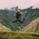 A woman jumps in the air with mountains and valleys in the foreground.