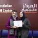Manar Amro holding a certificate with another person at The Palestinian Center