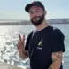 Bastien smiles and holds up a peace sign on a sunny day in front of the ocean