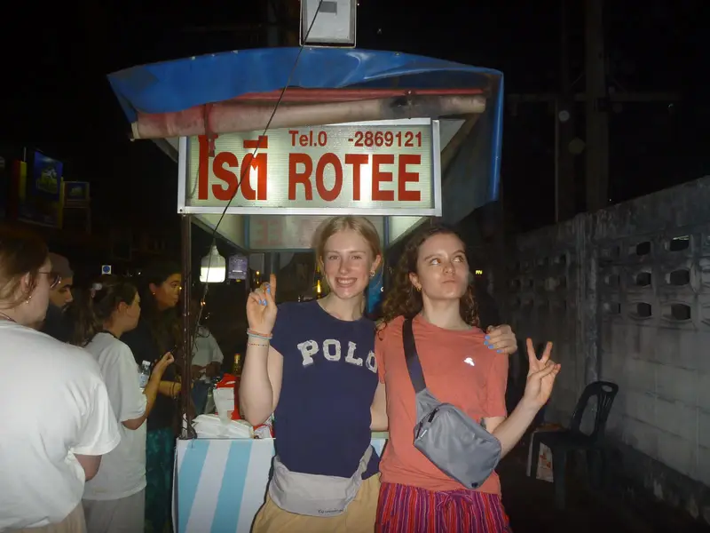 Two girls standing in front of a rotee street food cart 