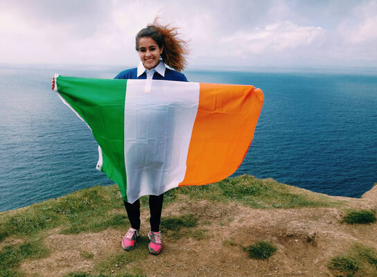 A student poses on a cliff with the Irish flag