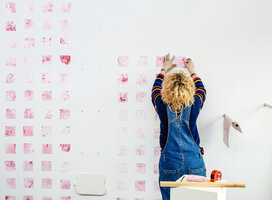 Student working on a piece of art, pink squares on a wall.