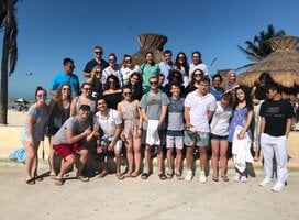 A group photo of participants in front of a hut on the sunny beach