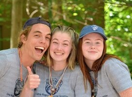 Image of 3 young adults smiling together in the woods