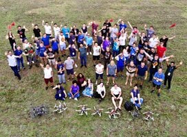 Students stand in a field with the drones they have just built and flown.