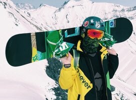Snowboarder holding board in green and yellow jacket with helmet