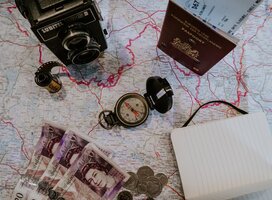 A camera, compass, passport, journal and currency on top of a map