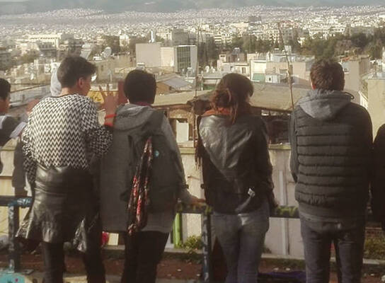 A group of students lined up a long a fence look at the view before them in Athens, Greece
