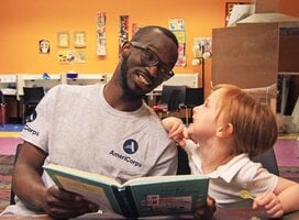 AmeriCorps member helping a young student to read. 
