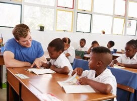 young male volunteer teaching English to young learners abroad