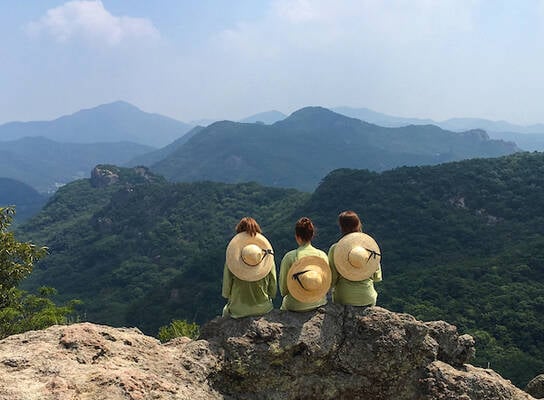 Three students sitting at the top of a mountain overlooking mountains in the distance