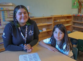 Reading Corps member with a student at a desk smiling