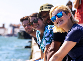 Summer students smiling on Venice canal wall.