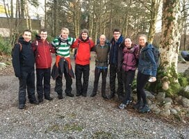 Group of young people in hiking gear. Standing in a line with arms linked, looking happy.