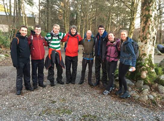 Group of young people in hiking gear. Standing in a line with arms linked, looking happy.