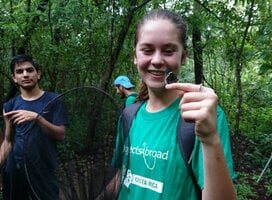 Teen wearing Projects Abroad Tshirt, holding butterfly in forest