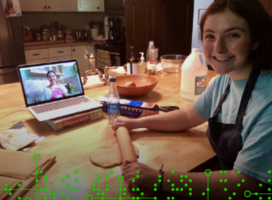 Image of a student with a rolling pin. A laptop in the background shows another student's face. 