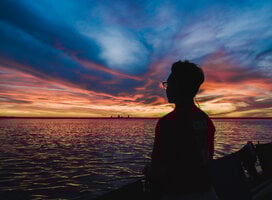 Silhouetted person looking out over the ocean during dusk.