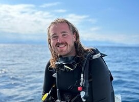A happy male diver sitting on the edge of the dive boat in full gear smiling at the camera