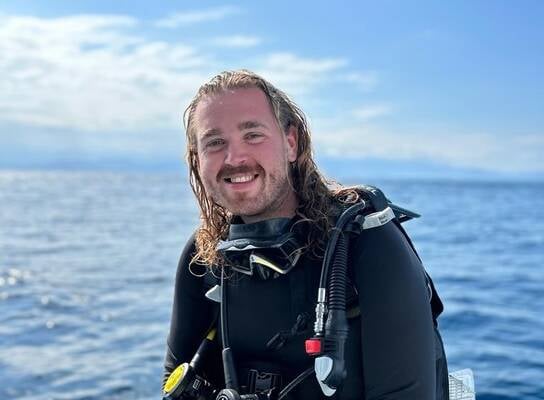A happy male diver sitting on the edge of the dive boat in full gear smiling at the camera