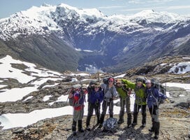 NOLS students stand for a photo in front of a snow capped peak