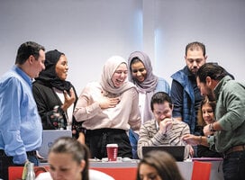 A group of male and female adults crowd around a laptop screen
