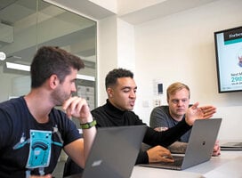 Three male postgraduate students work on their laptops in a meeting room