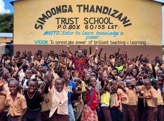 Volunteer cheering with children outside Simoonga. 