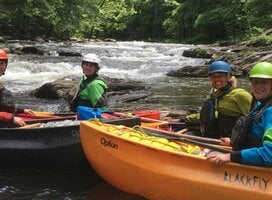 Crew in kayaks on a white water river, on the river bank look over for a picture.
