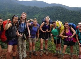 Crew poses for picture on a red dirt trail against background of lush mountain valley.