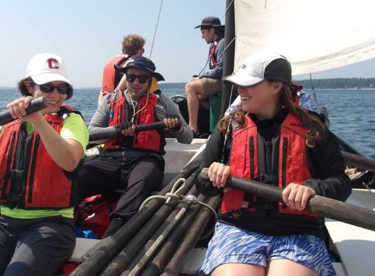 Students in a sailboat maneuvering oars.