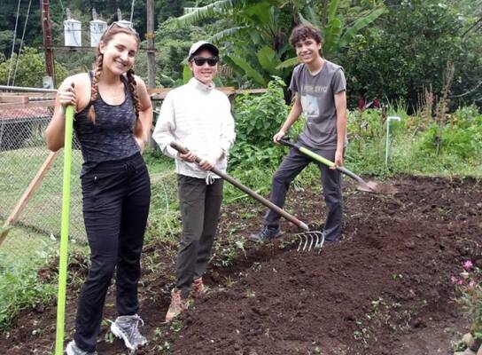 Three students pose for a picture holding gardening tools as they work on a service project.