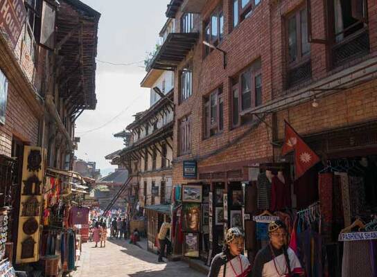 A traditional street scene in Kathmandu with local shops and two people in traditional attire.