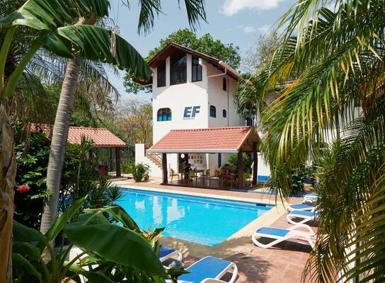 EF Tamarindo campus in Costa Rica with a pool surrounded by palm trees, lounge chairs, and tropical buildings where students live and study abroad.