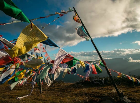 Prayer flags flying in the wind in the mountains of Bhutan with large clouds above in a light blue sky