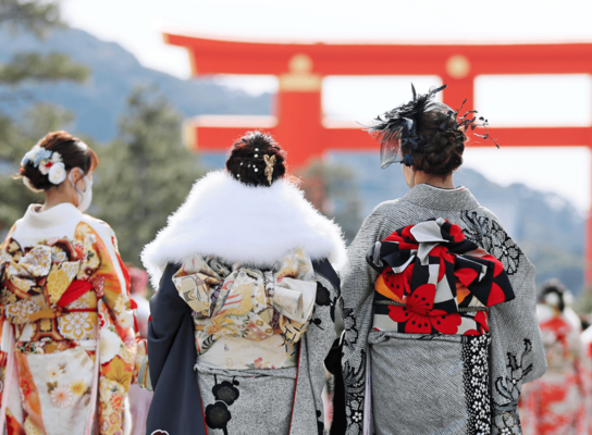 Traditional geisha walk towards a large torii gate in Japan