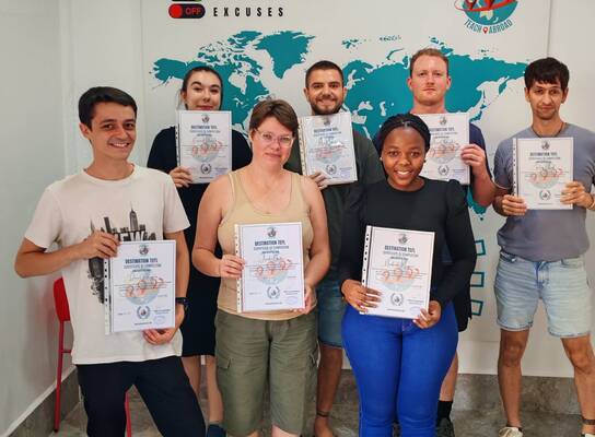 TEFL trainees holding certificates during graduation ceremony in training classroom.