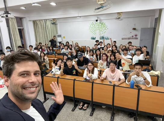 Smiling male TEFL teacher takes a selfie with a classroom full on students.
