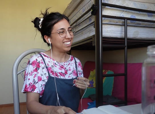 Smiling female TEFL teacher in bedroom teaching English online.