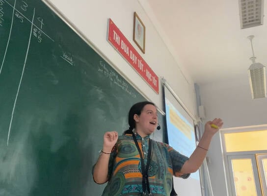 Female TEFL teacher in action wearing microphone and gesturing with hands.
