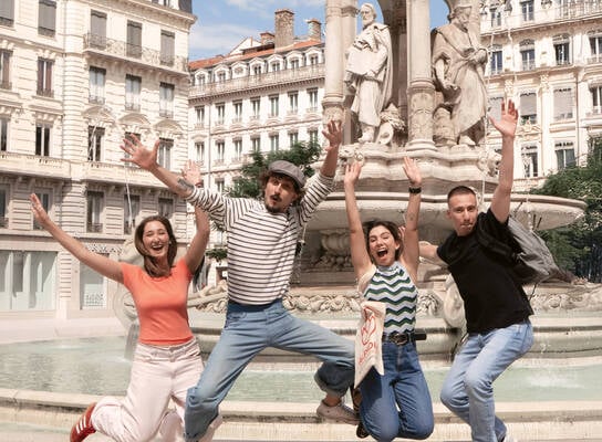 four people jumping in front of a historic fountain