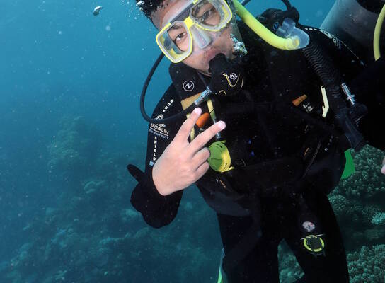 Jayden in Australia scuba diving underwater, wearing diving gear and posing his fingers in deuces