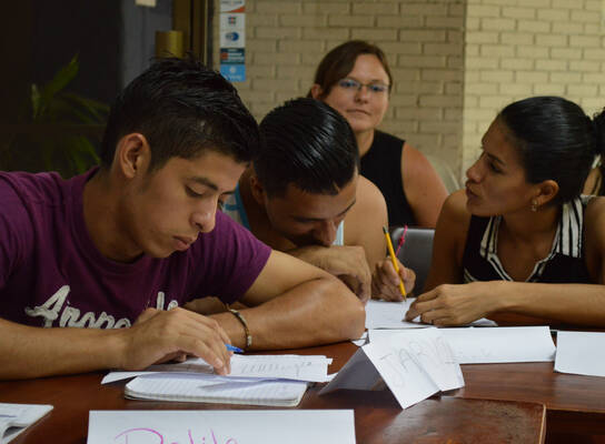 People working with worksheets around a wooden table.