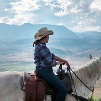 a girl in a cowboy hat rights a horse in the Canadian mountains