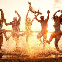 Happy people splashing in the ocean at sunset.