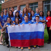 group of students in blue shirts holding large Russian flag
