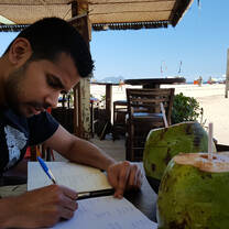 man writing on notebook with coconut drink